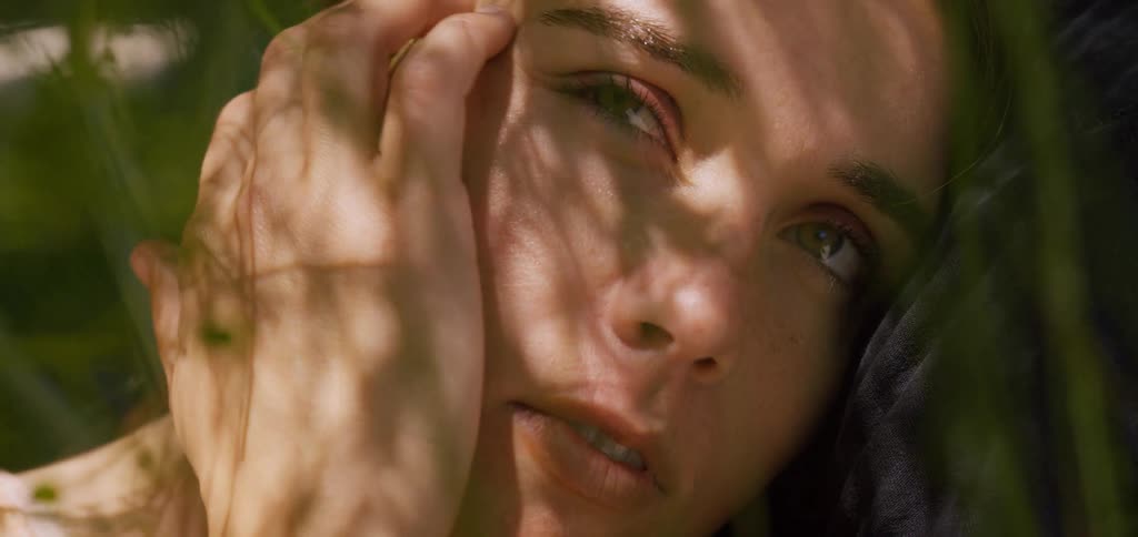 A close up of the face of a woman with green eyes and brown hair as she looks up with a partial shadow across her nose and cheek