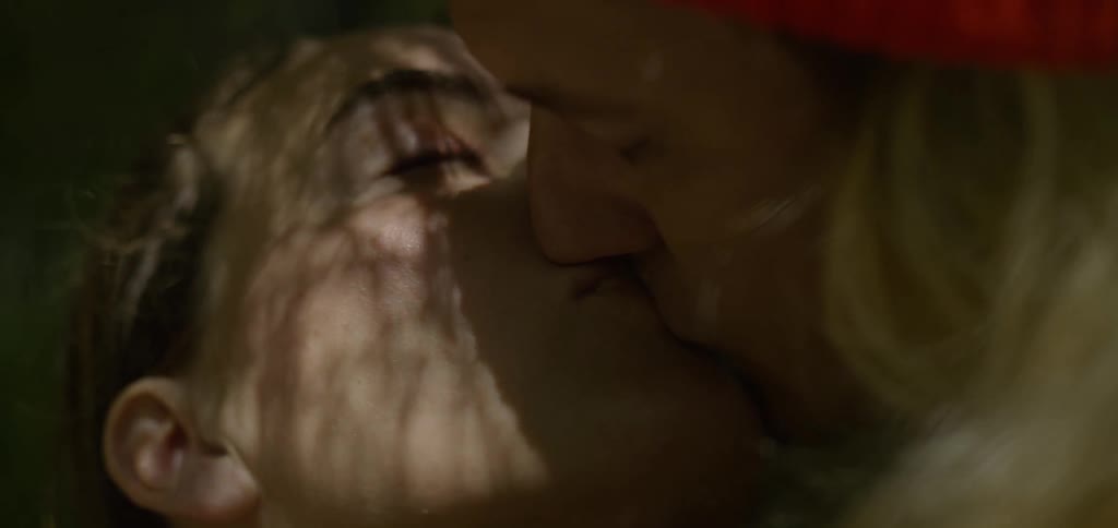 The video shows an intimate closeup of a couple sharing a kiss the camera focuses on their faces highlighting the moment as their lips meet with soft sunlight filtering through leaves and casting shadows on them
