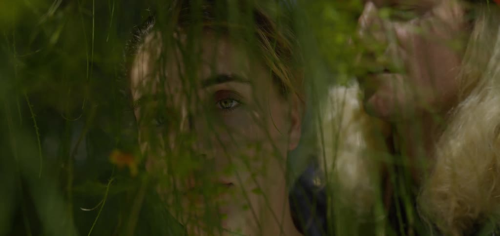 Two people among green leaves one looking upward and the other in profile partially obscured by foliage