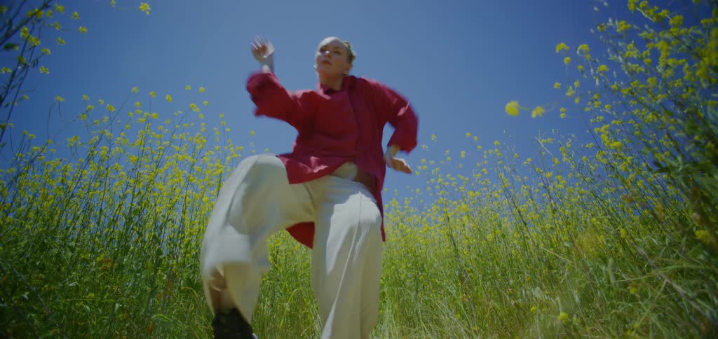 A young woman dances outdoors in a flower field during daytime