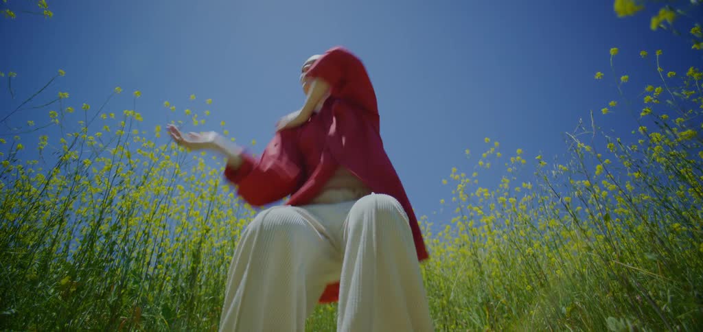 Blonde woman dancing against a blue sky in a field of yellow flowers