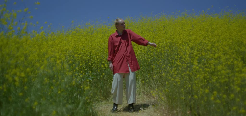 Blonde woman dancing outdoors against a clear blue sky
