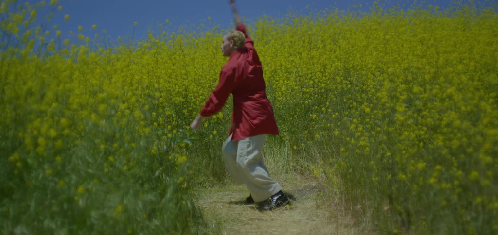 Blonde woman on a trail of a field of yellow flowers dancing