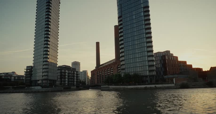 Modern buildings surround an old brick power station by the river at sunset