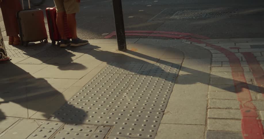 People cross a busy street with suitcases and shopping bags under sunlight