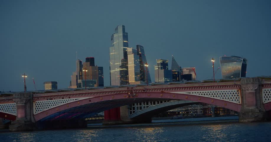 A bridge connects city neighborhoods with a series of highrise and skyscraper buildings in the background at sunset