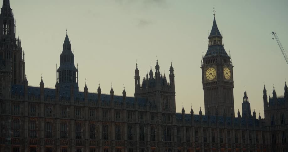 The palace of westminster in london with the big ben clock tower visible at sunset and a crane in the background