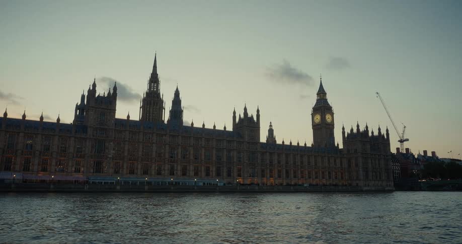 The palace of westminster in london stands beside a river with the big ben clock tower visible at sunset