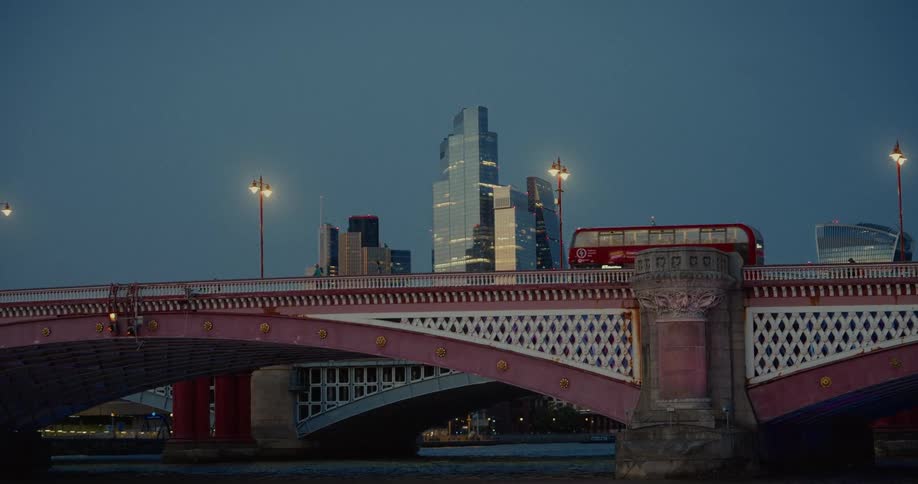 Red bus crosses an illuminated bridge in london with skyscrapers in the background