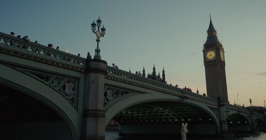 The Big Ben stands just beyond Westminster bridge filled with pedestrians in the city at sunset