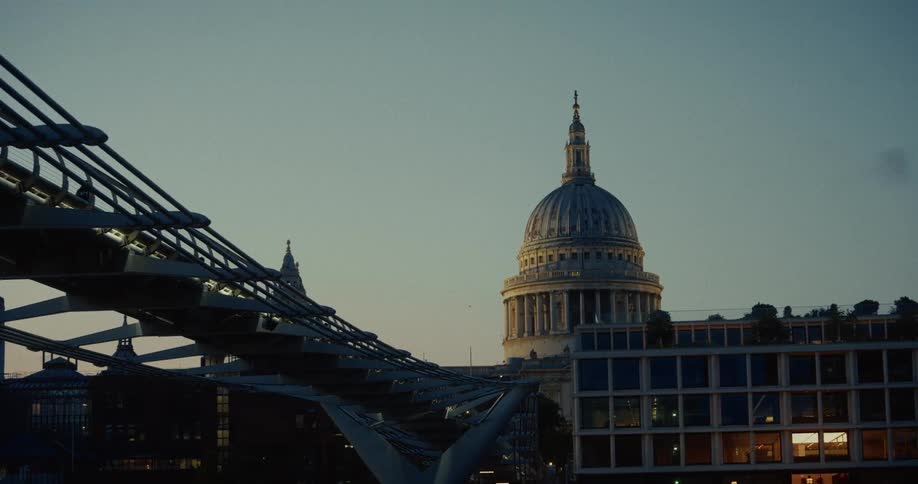 St Pauls cathedral rises behind a modern steel bridge structure on the left side of the frame all viewed under a pale twilight sky with faint purple and blue hues