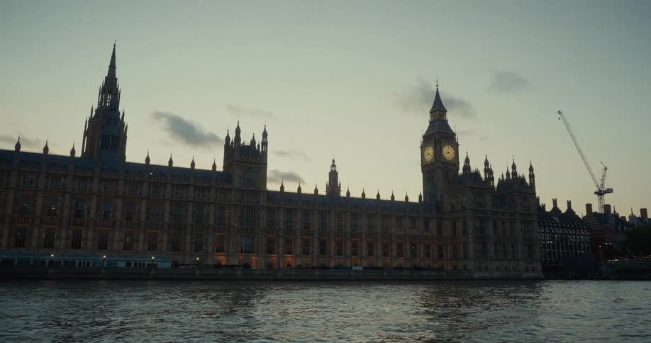 The video shows the palace of westminster in london england viewed from across the river thames at dusk the iconic big ben clock tower is visible with a construction crane behind it