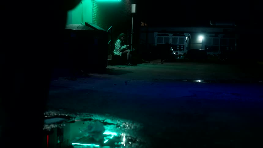 Three people surrounding a woman in an alley at night