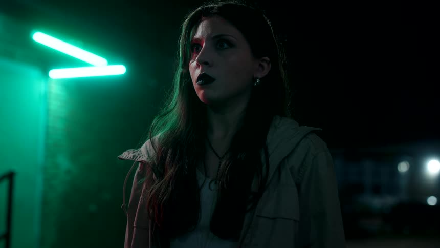 A young woman standing in the street at night looking surprised and scared