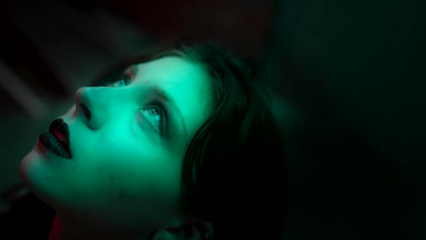 Female face lit by green light looking upward with an intense expression