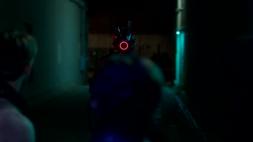 A man wearing a robotic helmet with red lights is suddenly attacked by three street thugs in a dark alley at night