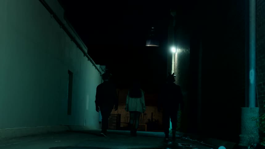 Three people walking in an alley lit by blue lights at night