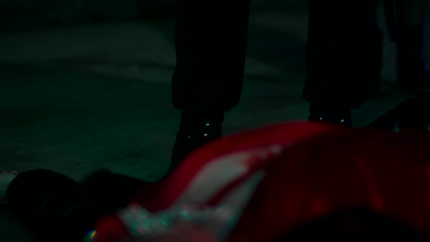 The video shows the lower half of two peoples legs and feet walking on a pavement at night the ground is lit with blue and green light from an unknown source