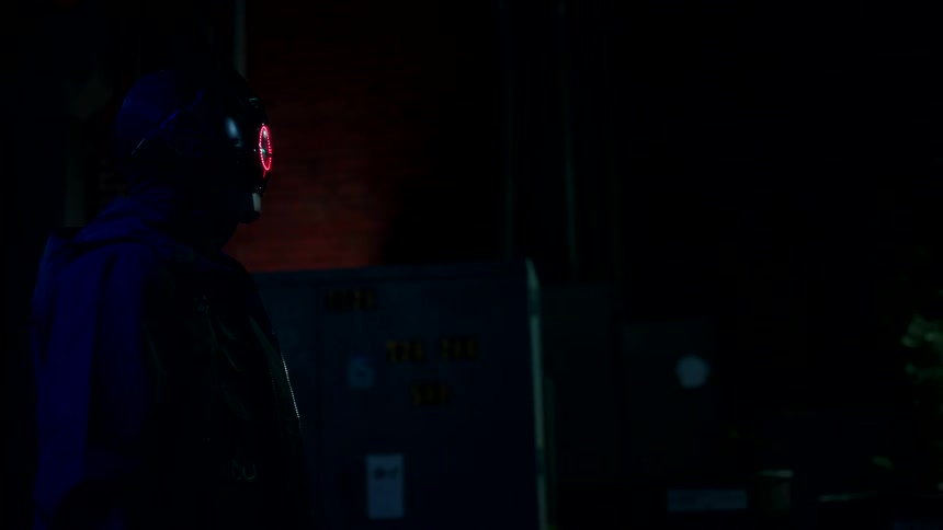 A man wearing a robotic helmet walks down the street at night