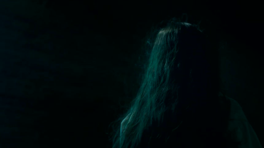 A young woman walks alone in a dark alley filled with fear as a nearby building door is illuminated by fluorescent light