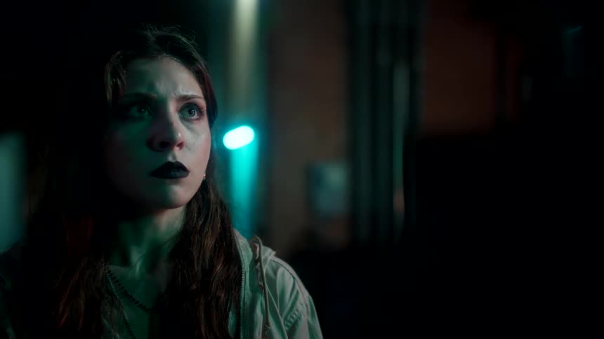 Young woman faces someone in the darkness of an alley with a tense expression