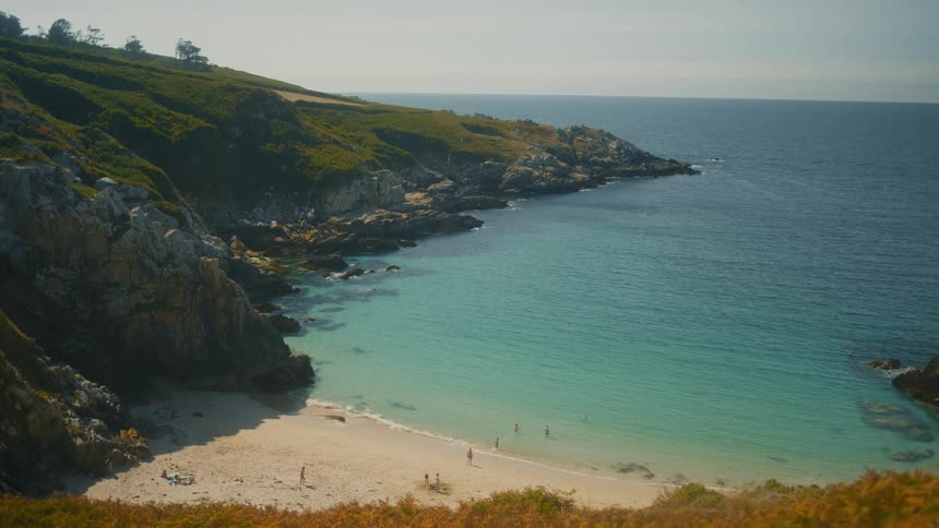 A group of people have fun on the beach at midday with the shoreline bordered by rocks