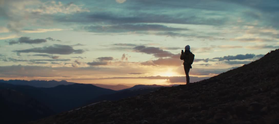 Person with a backpack watches the sunset from the mountain top
