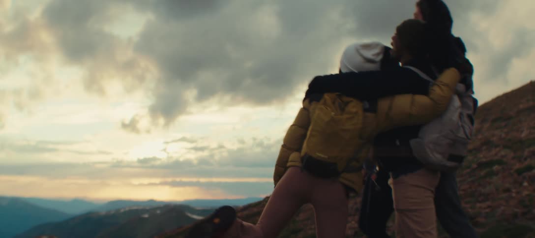 Group of friends hug at the top of the mountain enjoying the sunset view together