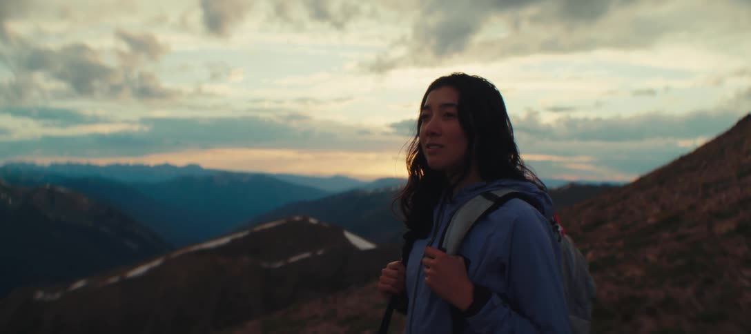 Woman with a backpack contemplates the mountainous landscape at sunset