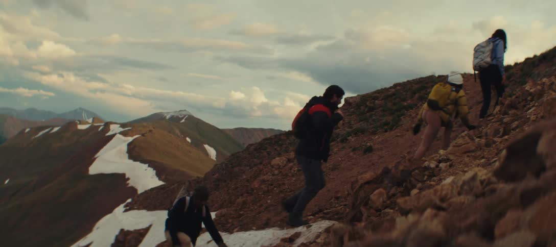Four people are hiking up a rocky mountain at sunset