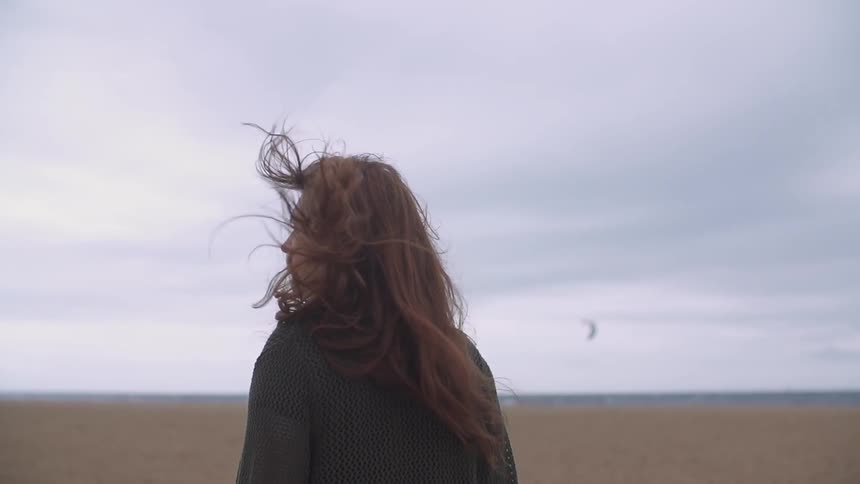 Woman walking on a beach with her hair blowing in the wind