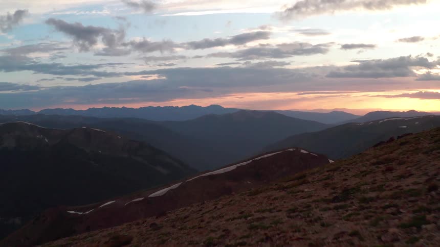 Three hikers trek up a mountain slope at sunset
