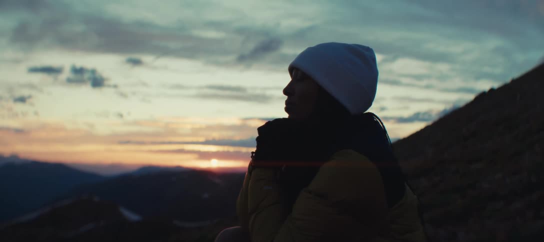 Close up of a young black woman sitting on a mountain slope outdoors at sunset