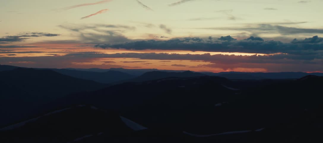 Silhouettes of mountains under an orange sunset sky