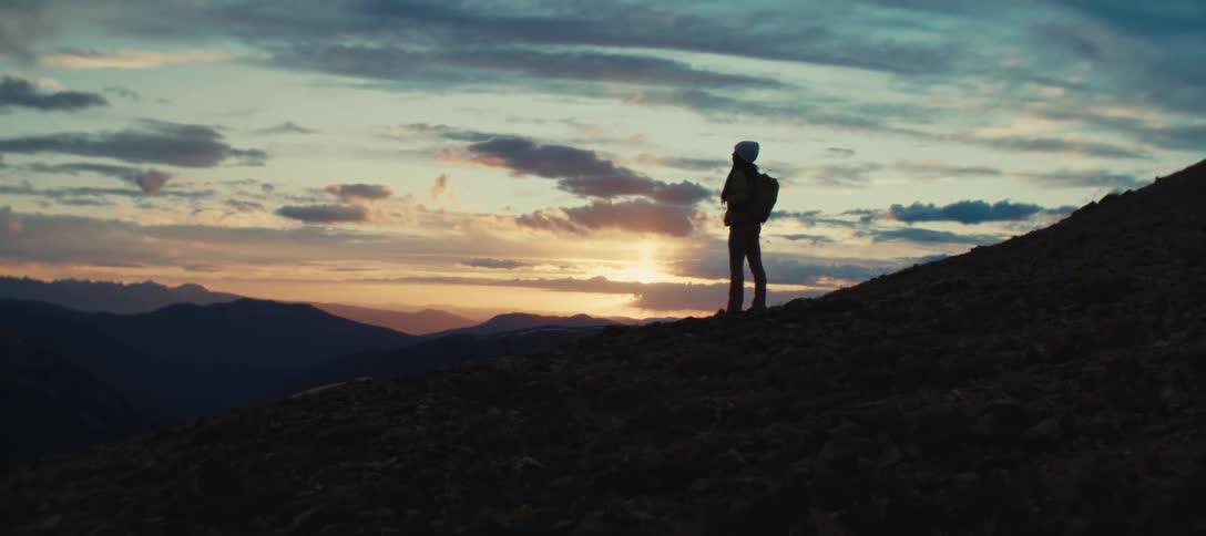A person standing in an outdoor environment that is dark in the morning looking at the horizon where the sun is shining in the sky