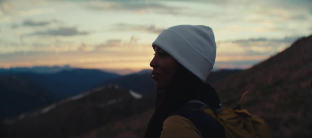 A woman wearing a white cap is standing looking at a landscape with the sun shining in the sky for tomorrow