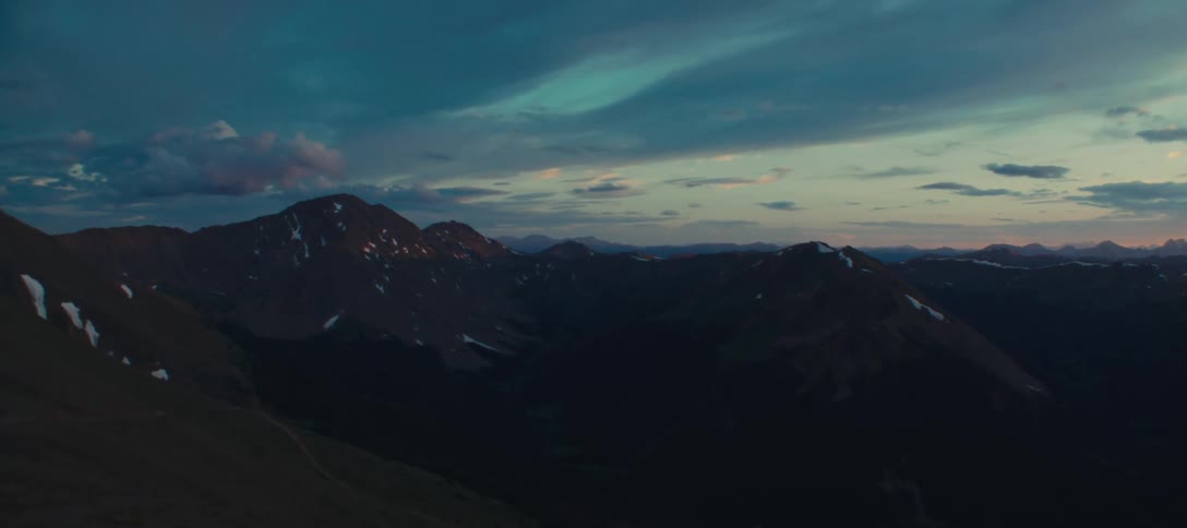 Mountain range at dusk with dark peaks contrasting against the blue sky and clouds lit by the sunset