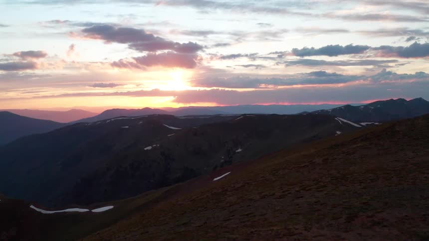 Group of four people walk along the mountain ridge as the sun sets on the horizon