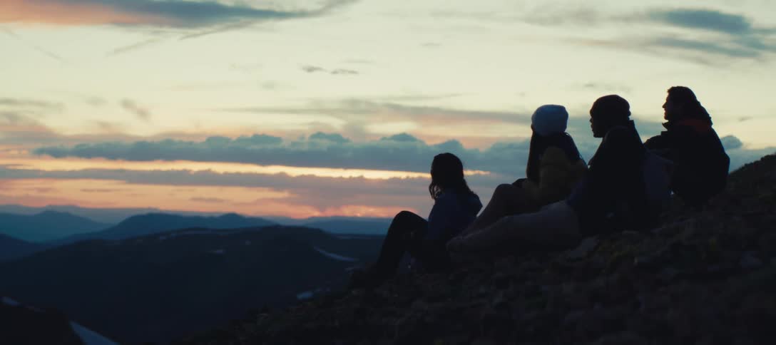 A group of four friends watch the sunset while sitting outdoors on a mountain slope