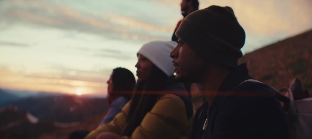 Three people wearing hats and warm clothing are sitting outside staring straight ahead
