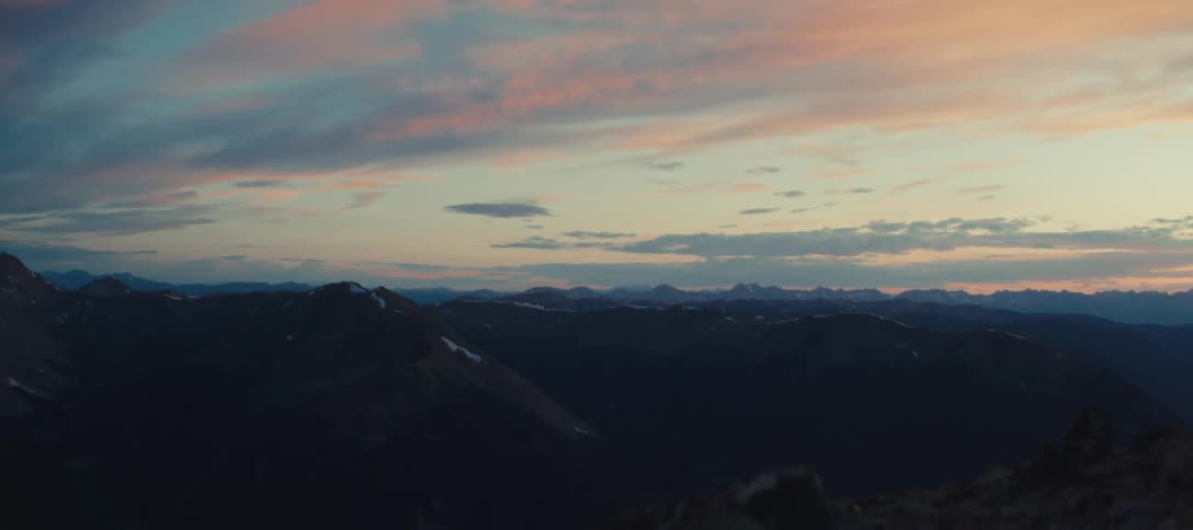 Dark mountain range with snow seen at sunset under a colorful sky