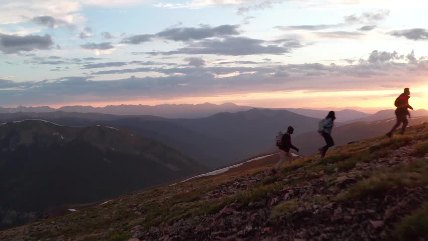 Three people hike up a steep mountain trail during sunset