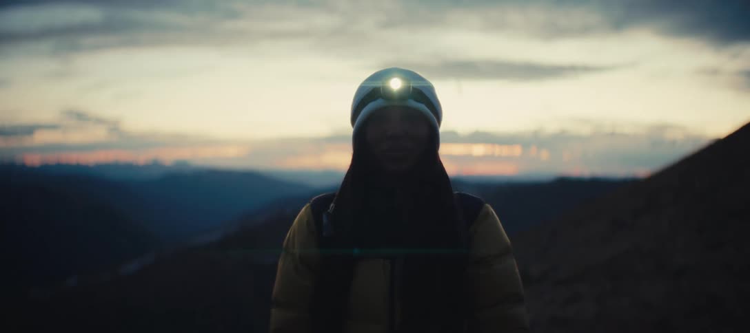 A woman with a flashlight attached to her head is standing outside at dusk