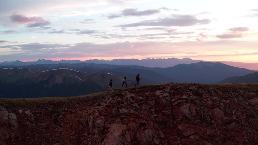 Three hikers walk along a ridge line in a mountain range at sunset