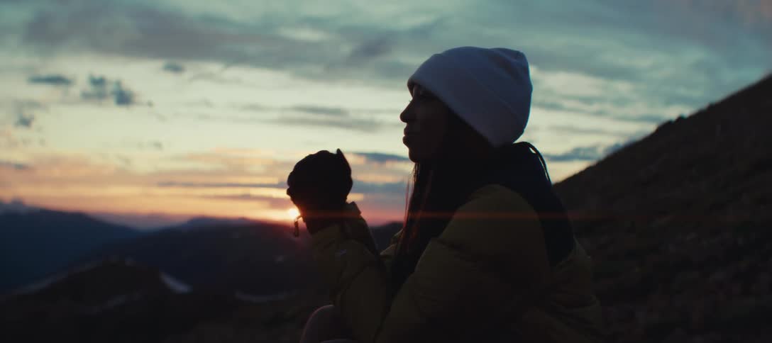 A young black woman sits on a mountain slope outdoors at sunset