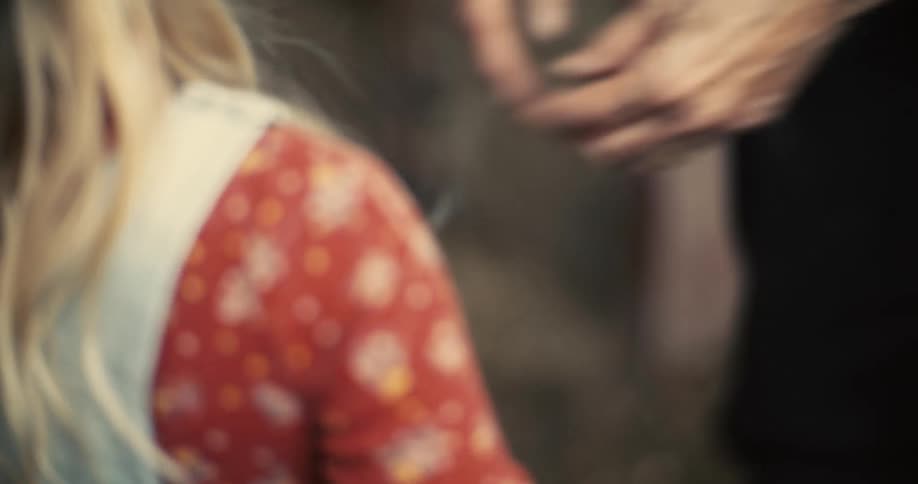 The video shows a blurry closeup of a persons hands and face with their movements largely obscured by the cameras shallow depth of field a second persons hands are visible in the foreground reaching towards the first person