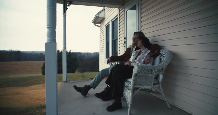 A couple sits closely together on a porch bench