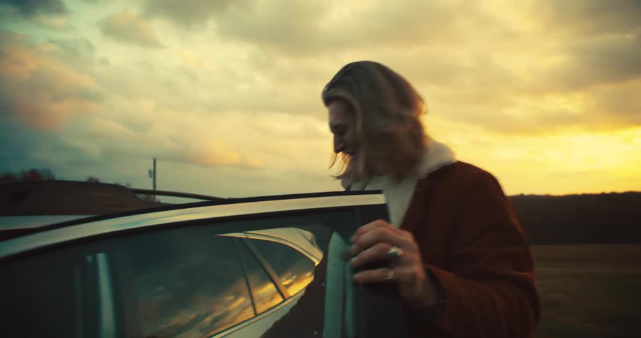 A man is stepping out of a car at sunset in an open field