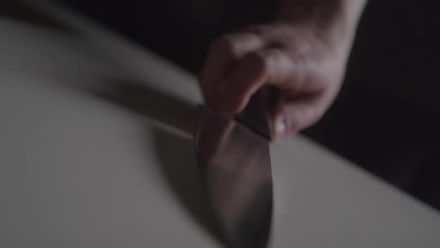 Hand holding a large knife resting on a light surface