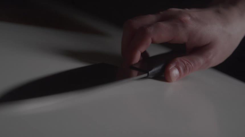A closeup of a mans hand as he slowly and deliberately unsheathes a large dark knife